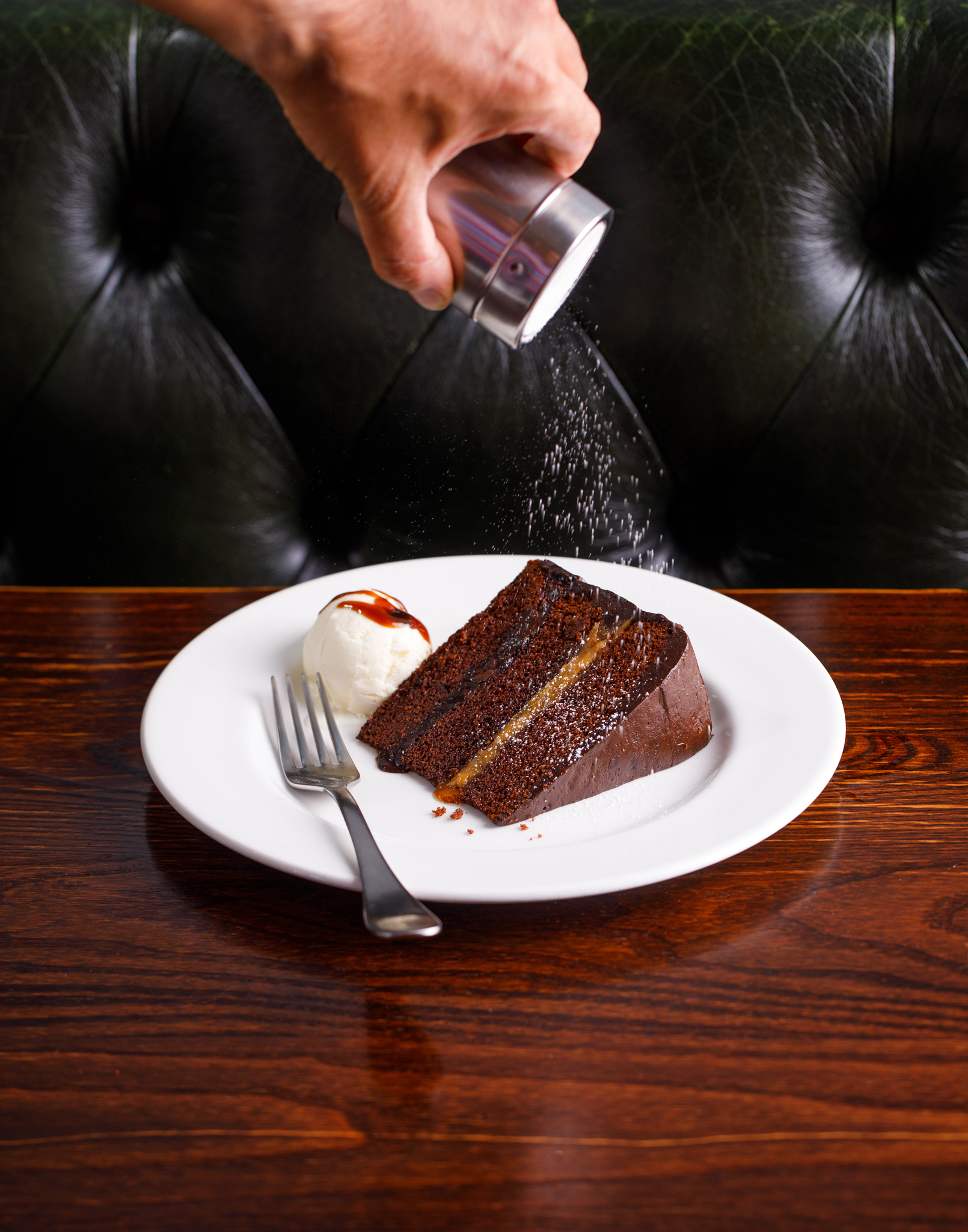 photo of a piece of chocolate cake being dusted with icing sugar from above