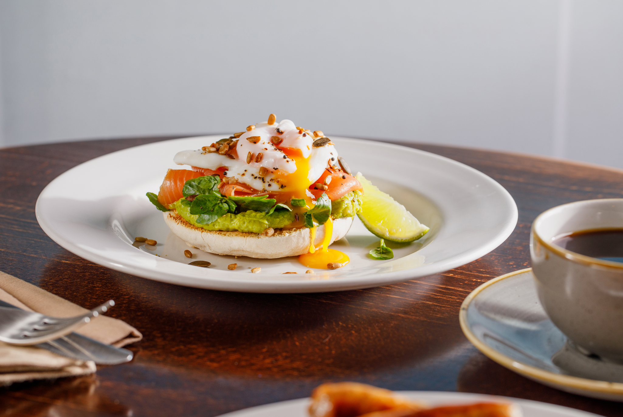 Photo of smashed avocado and smoked salmon on an english muffin, topped with a poached egg and the yolk is dripping down the side of the avocado