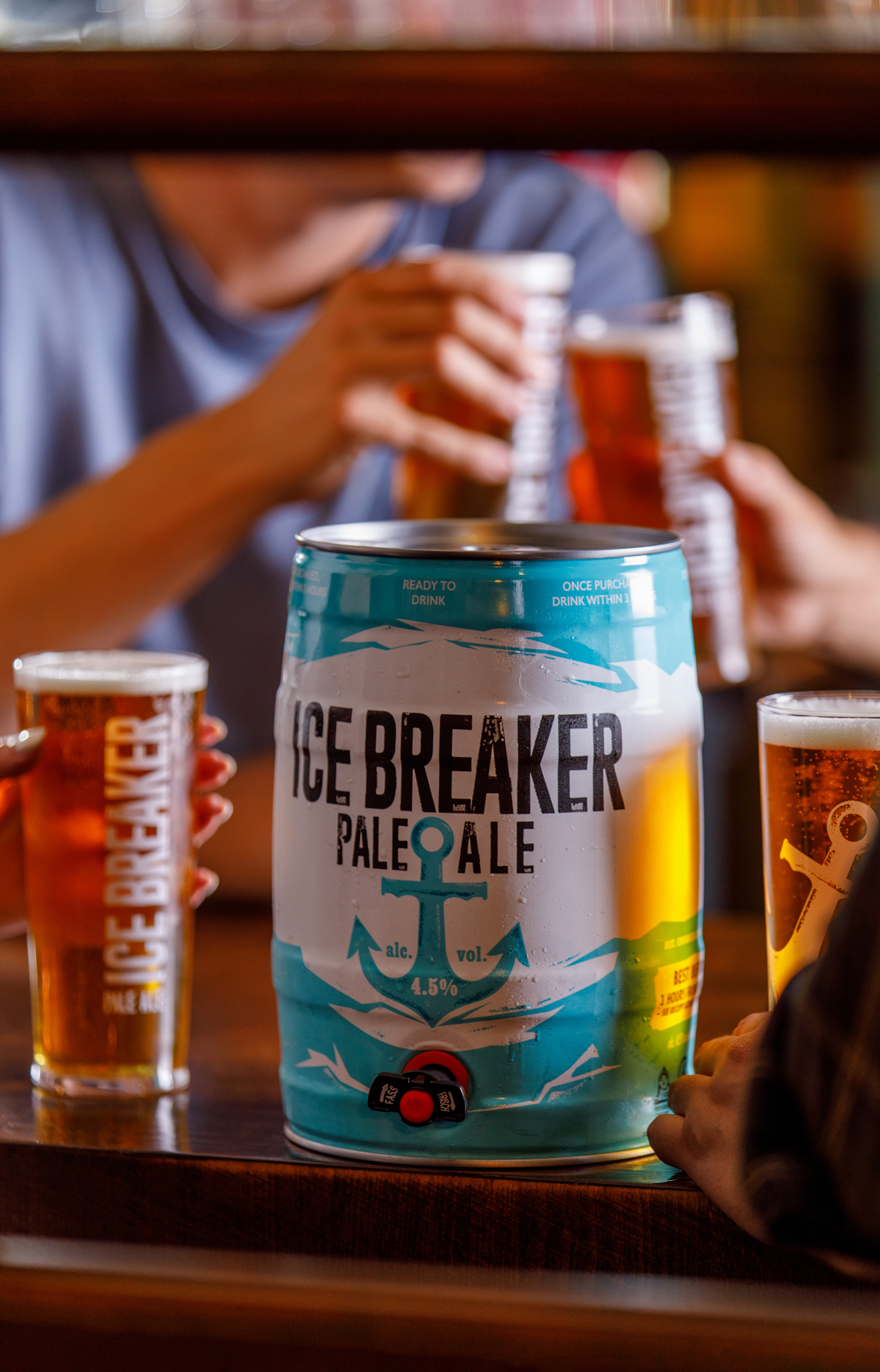 photo of small keg of ice breaker pale ale being shared with friends, people cheersing pints of beer in background