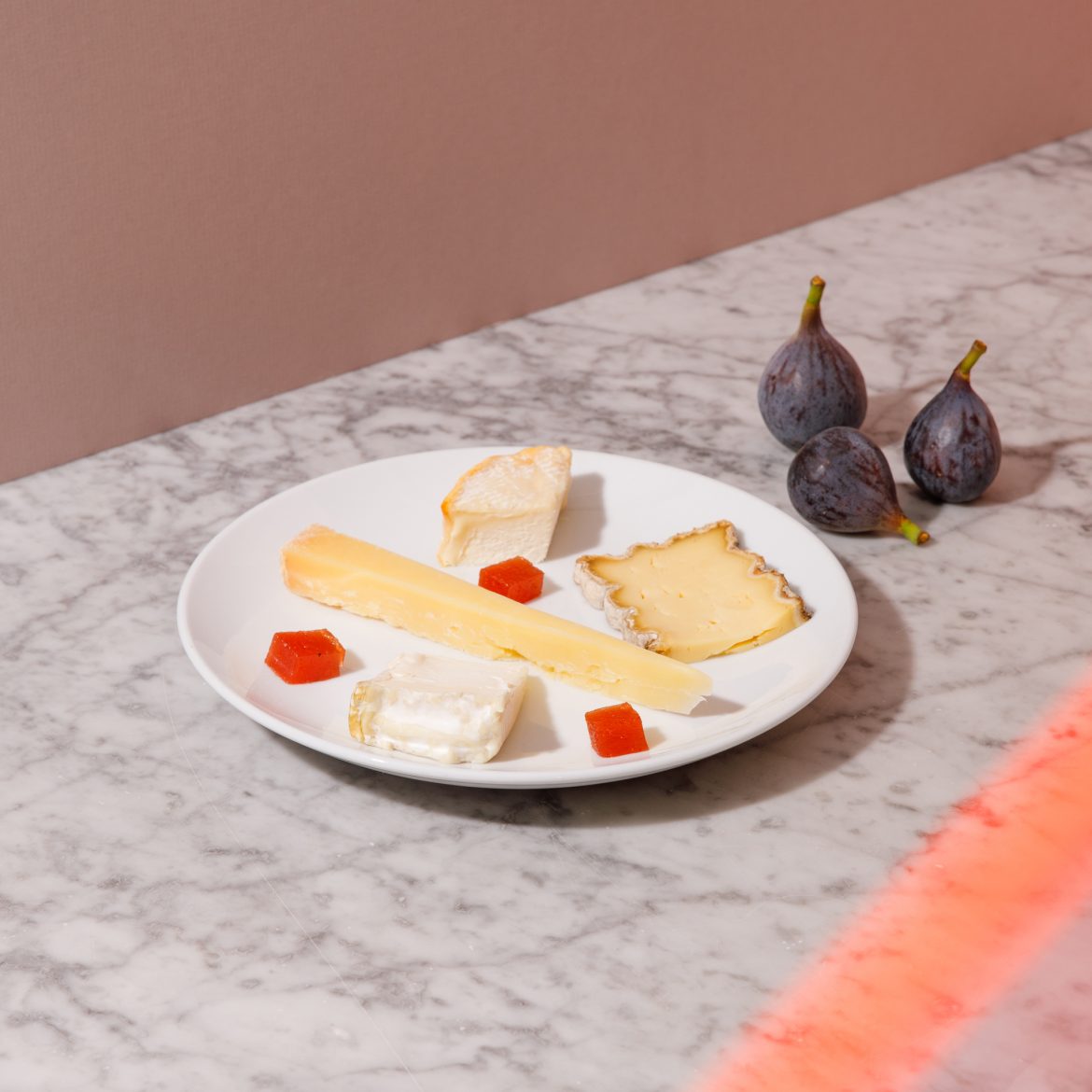 a plate of small pieces of cheese, abstract placement with 3 figs off plate in background. Background is marble table