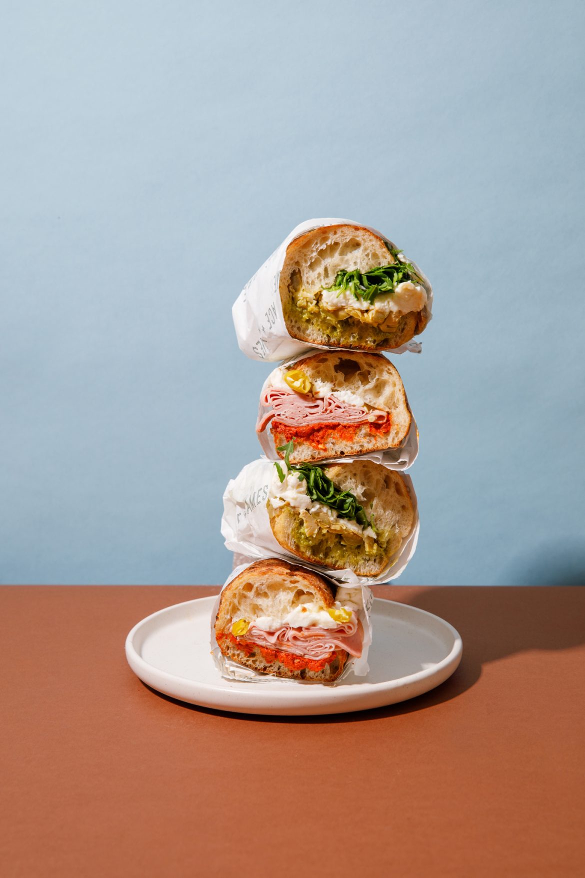 photograph of stack of sub style sandwiches. 4 sandwiches places on top of each other forming a sandwich totem pole