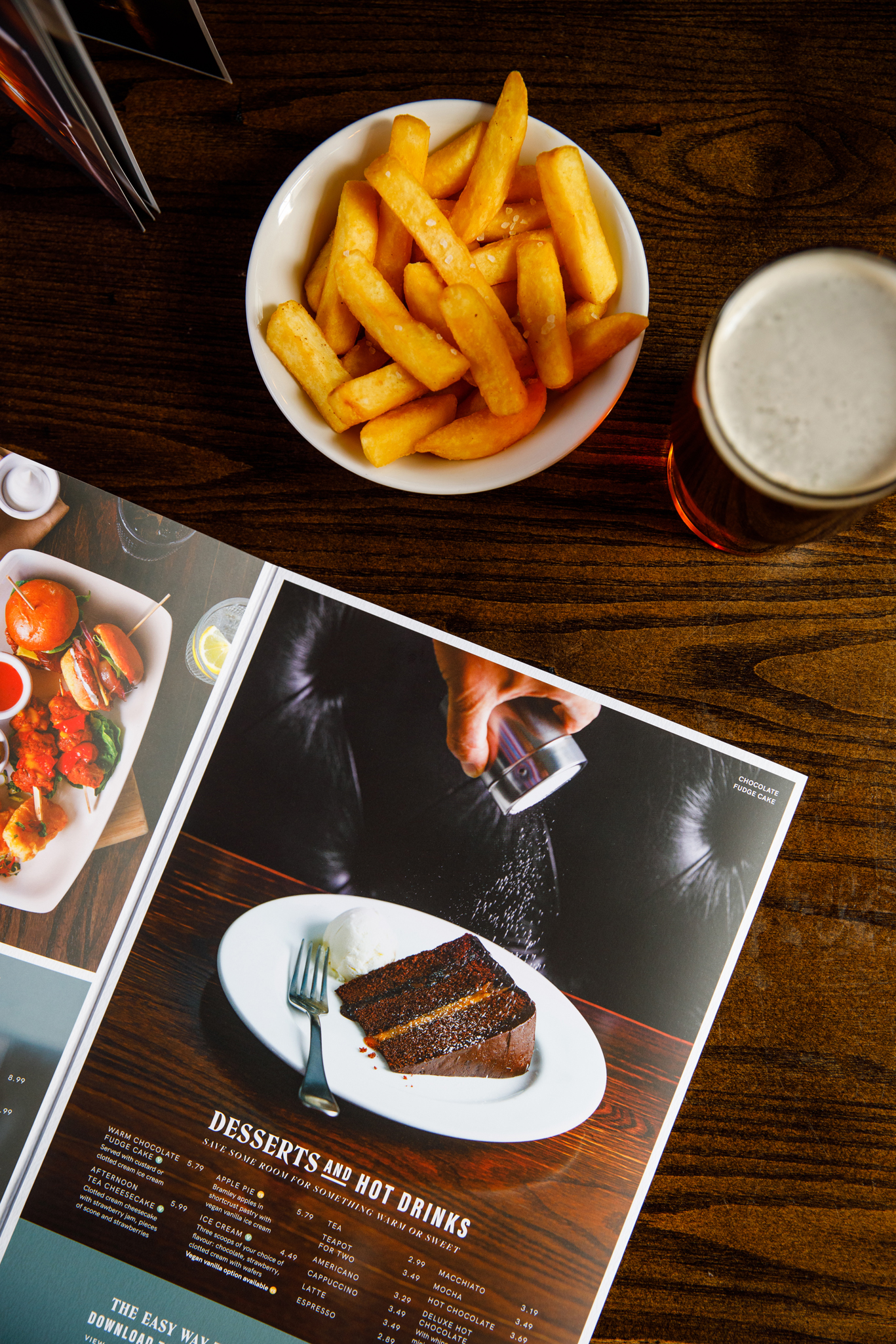 photo of a pub menu open on a table with a bowl of chips and a pint of ale