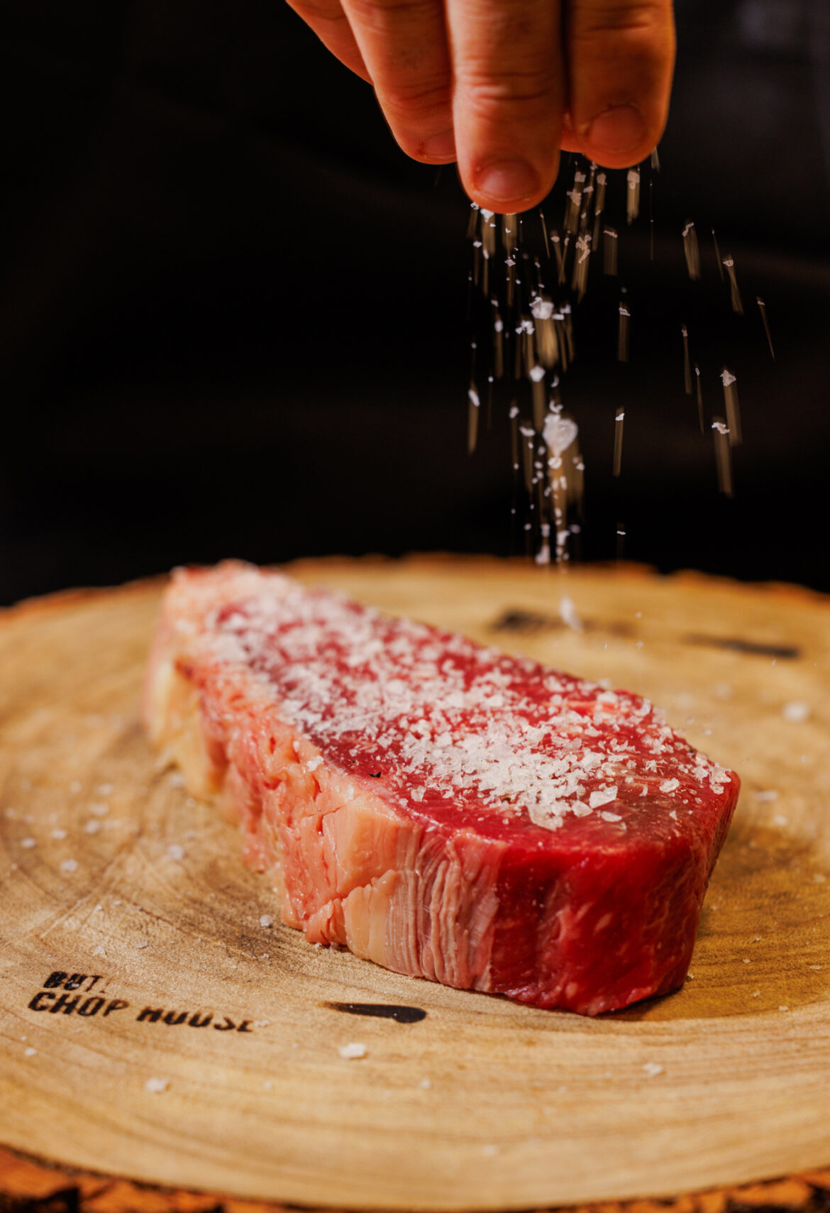 A raw steak being sprinkled with coarse sea salt