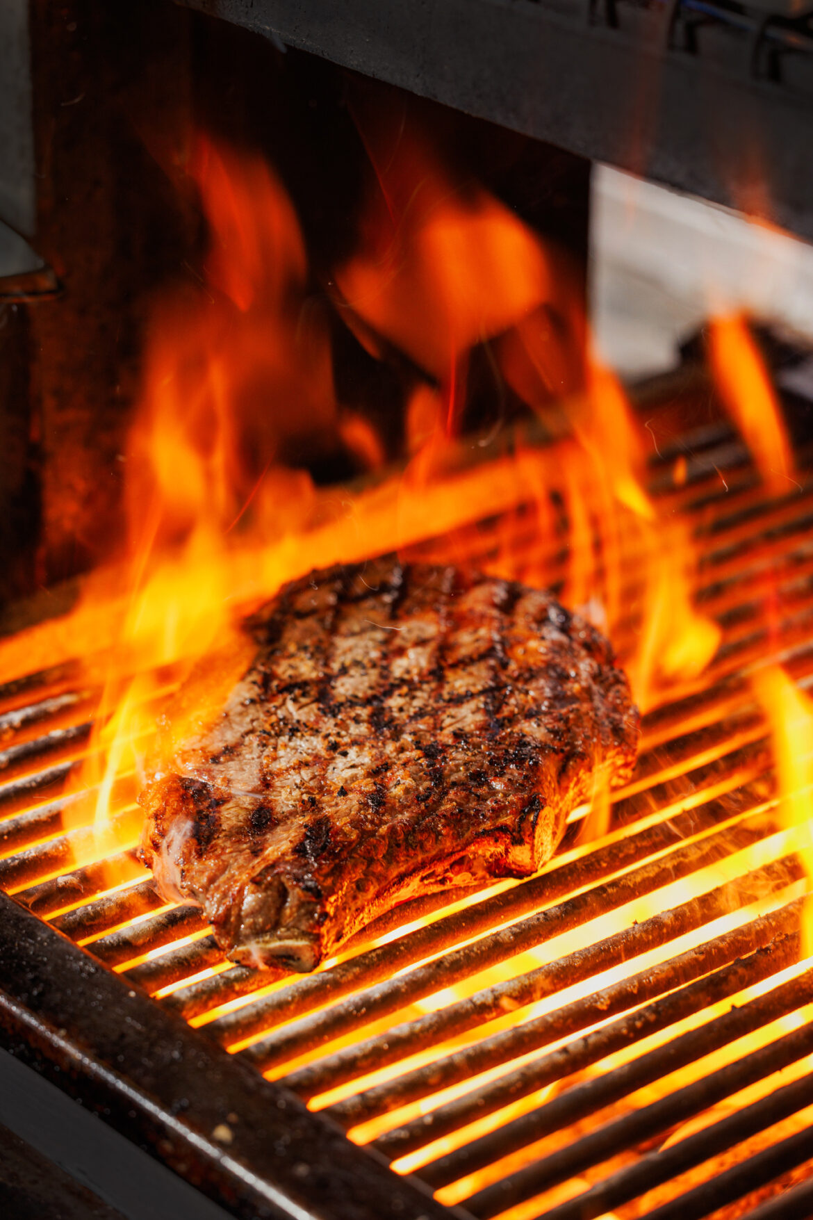 A photo of a steak on a char grill surrounded by flames