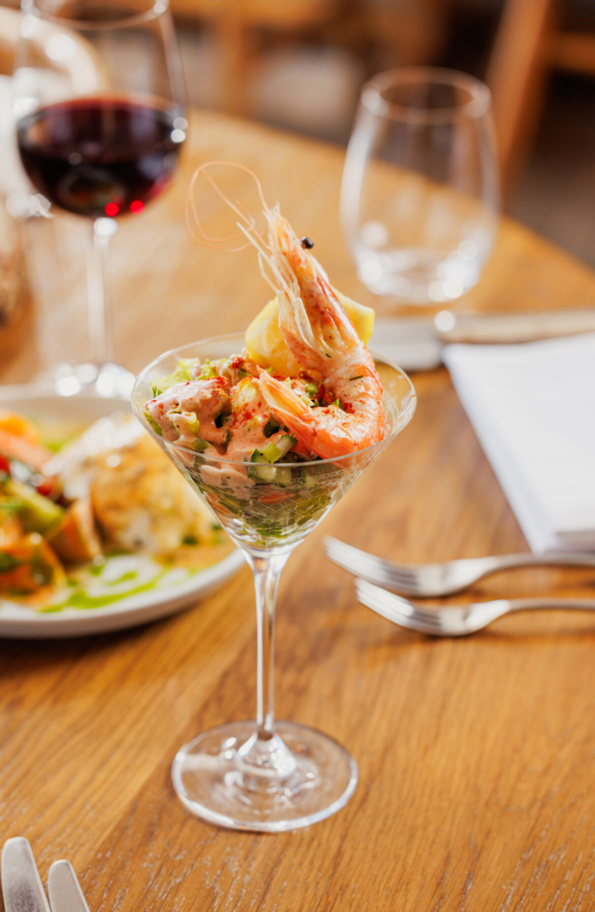 A plate of food on a table: A prawn cocktail served in a cocktail glass with a whole shell on prawn.