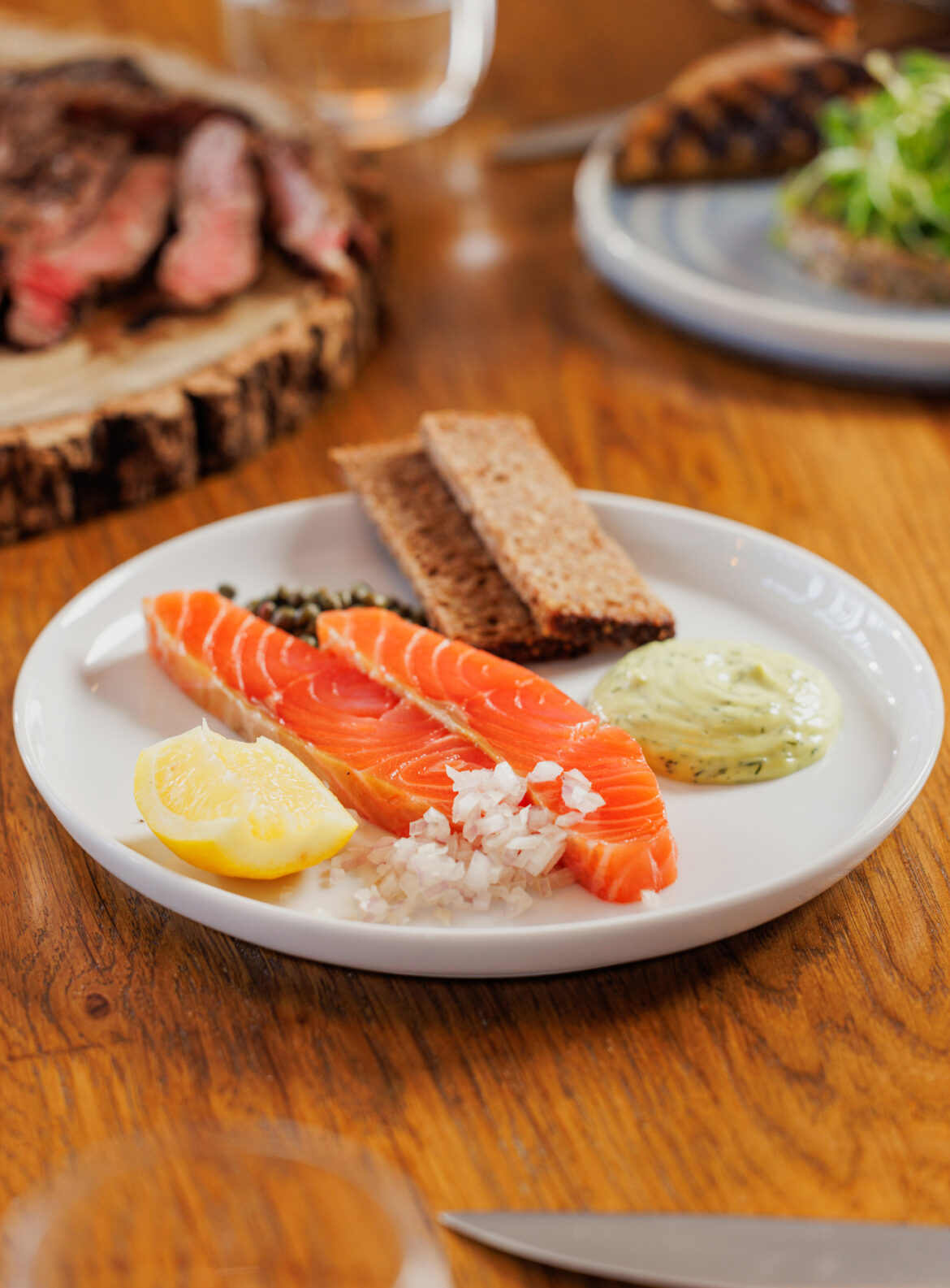 A plate of food on a table: smoked salmon, rye bread, a wedge of lemon and finely chopped shallots