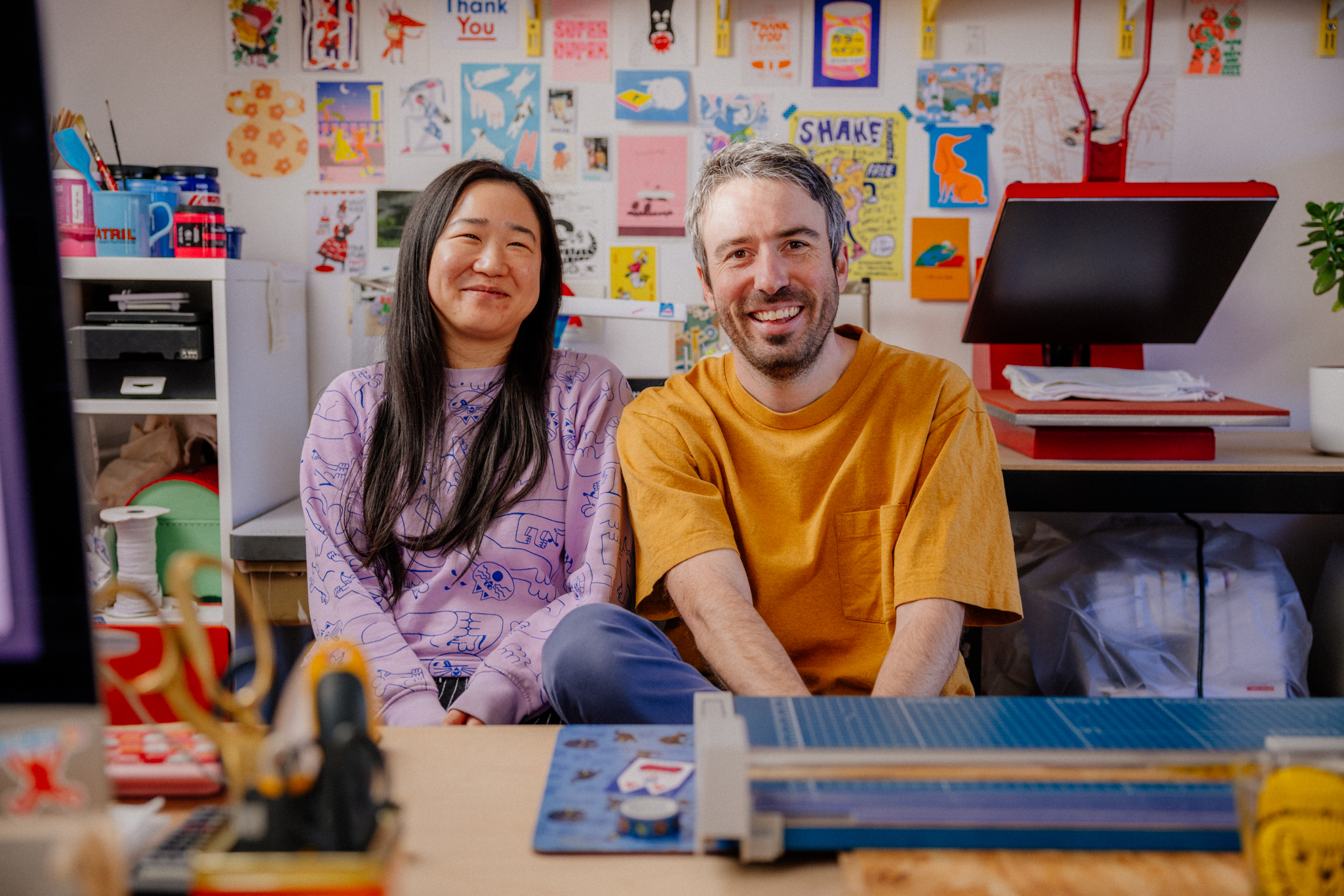 a portrait of two artists in their studio surrounded by creative ephemera