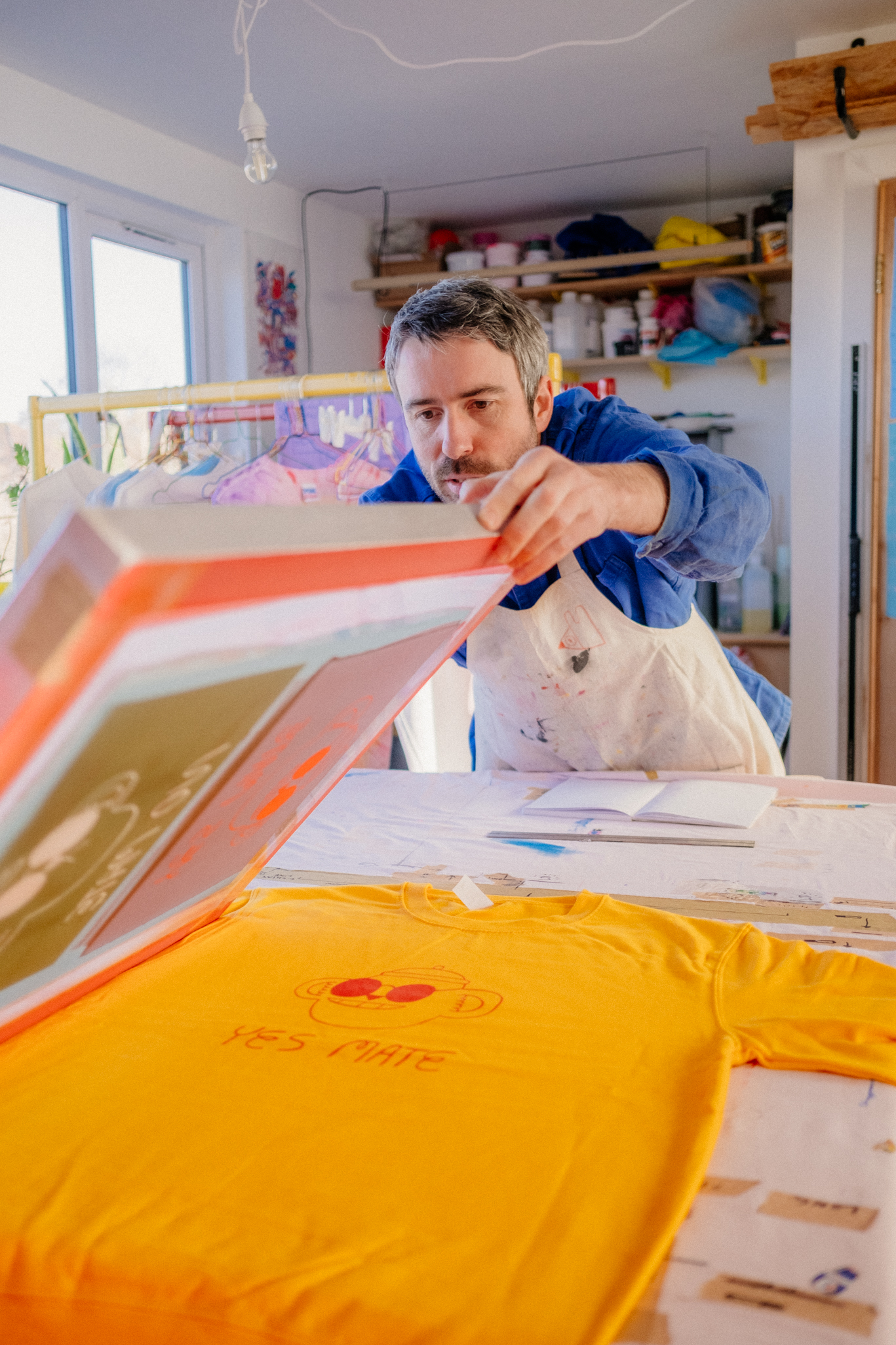 photography of a male artist screen printing a yellow t-shirt in studio
