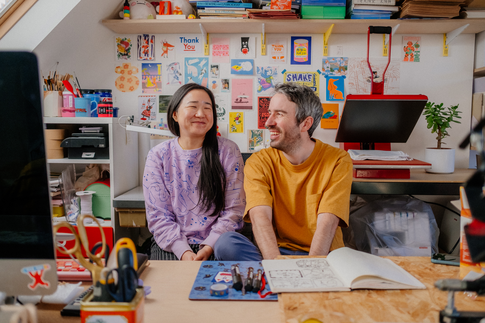 a portrait of two artists in their studio surrounded by creative ephemera