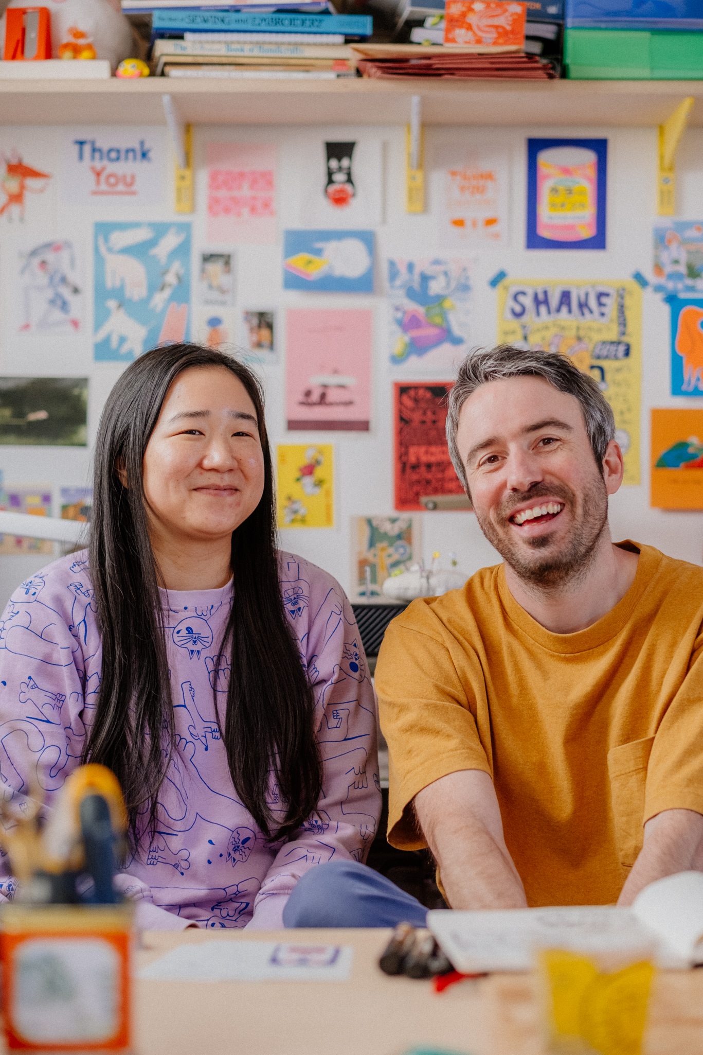 a portrait of two artists in their studio surrounded by creative ephemera