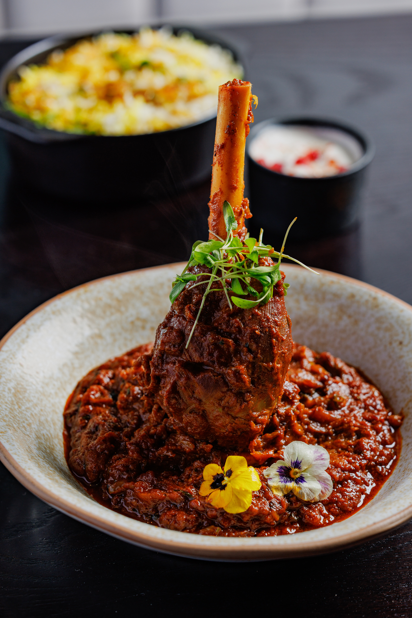 Slow-cooked lamb shank at Pravaas — Braised lamb shank served in a deep red sauce, garnished with edible flowers and micro herbs.