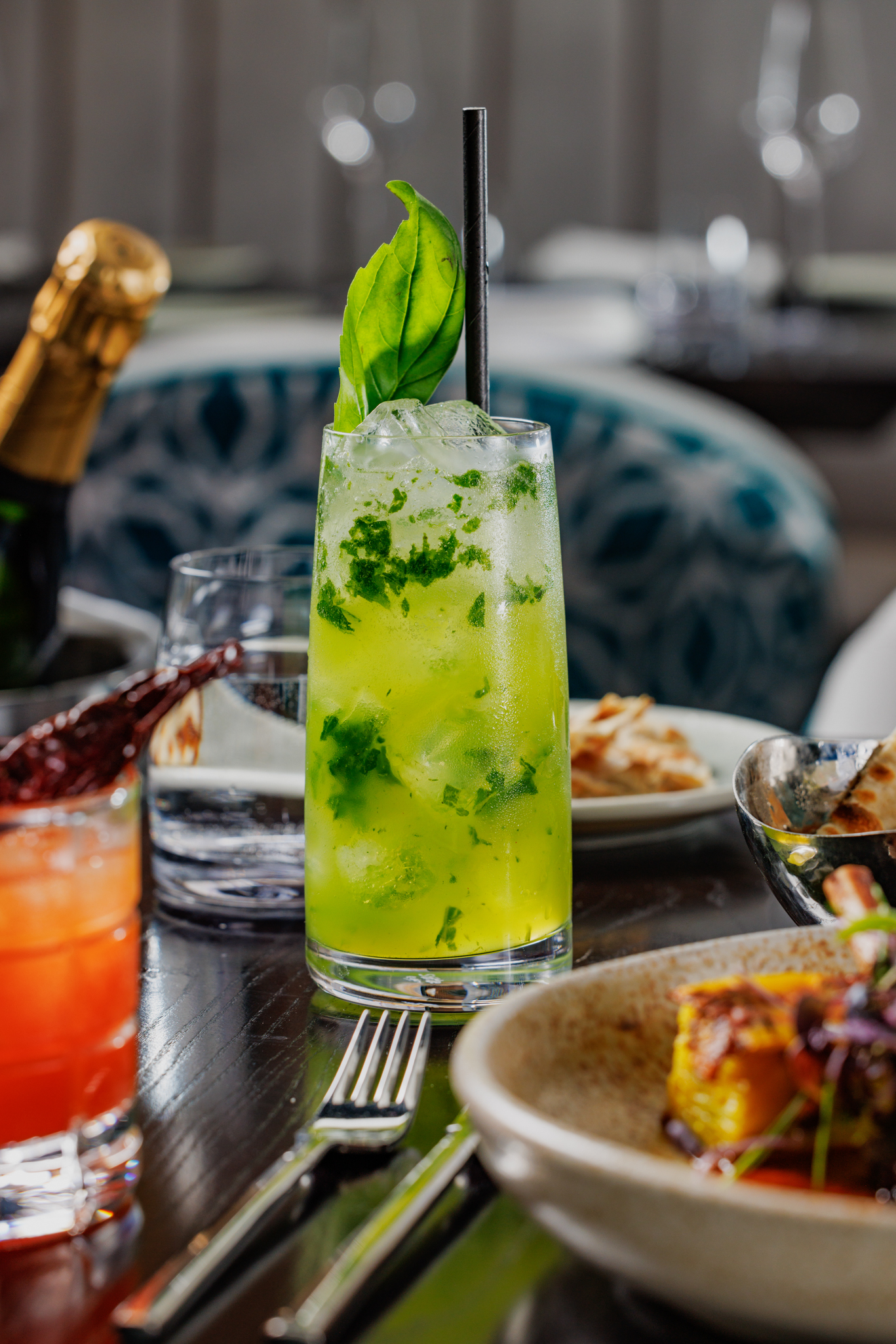 Bright green cocktail at Pravaas — Refreshing green cocktail with basil garnish, photographed among a busy table setting.