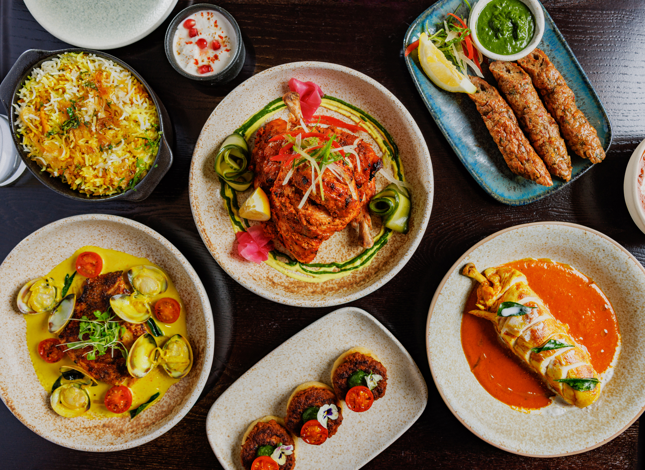 Flat lay of Indian dishes at Pravaas — Overhead view of a table full of vibrant dishes including biryani, tandoori chicken and curries.