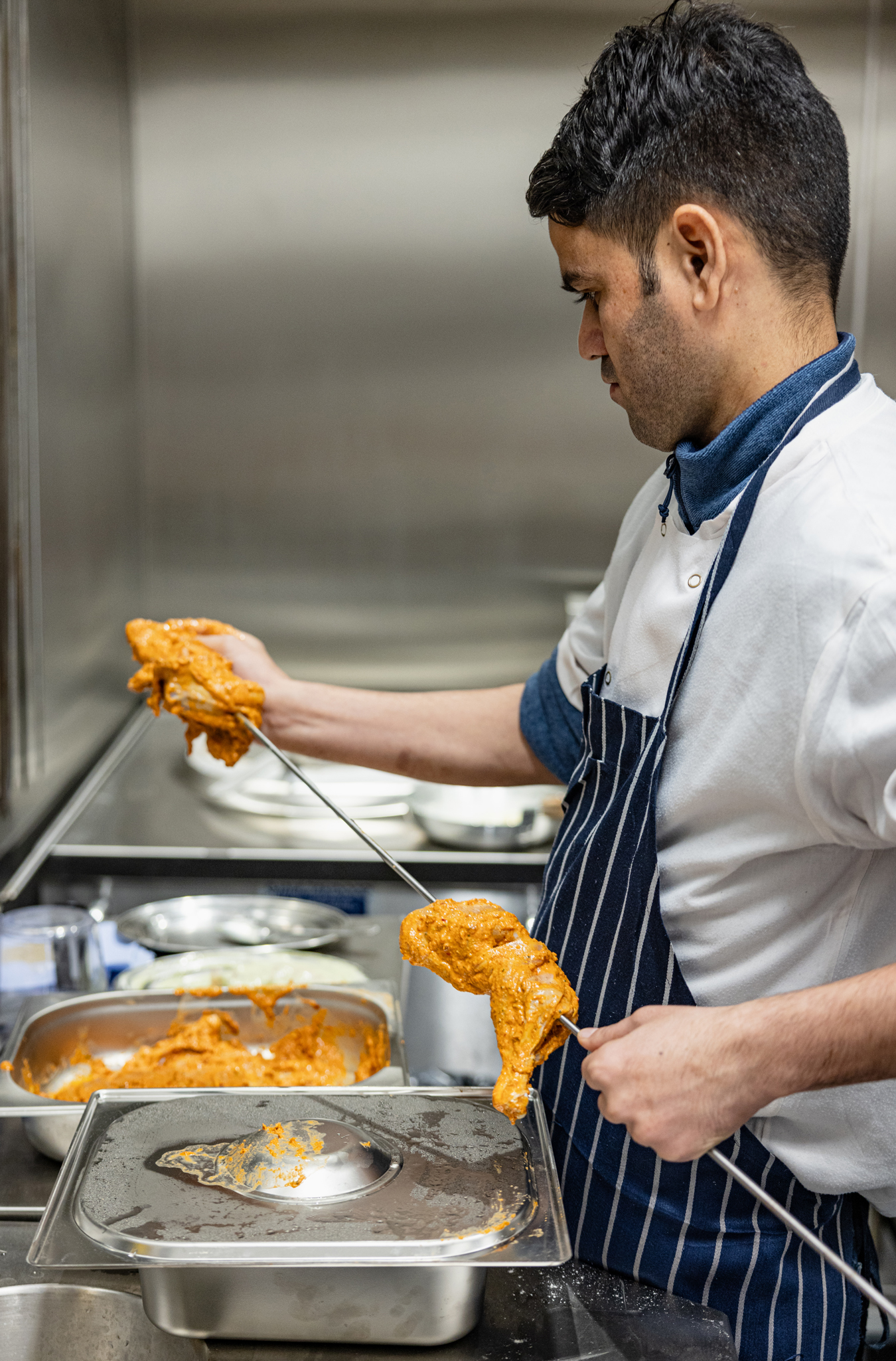 Chef preparing marinated chicken for the tandoor at Pravaas — Action shot of a chef threading spiced chicken pieces onto skewers in the kitchen