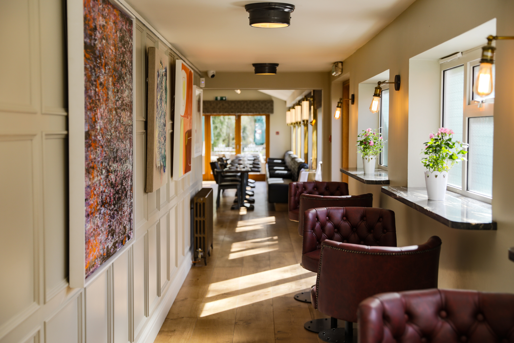 Stylish hallway lounge area at The Mount with leather chairs, natural light, and contemporary artwork on the walls.