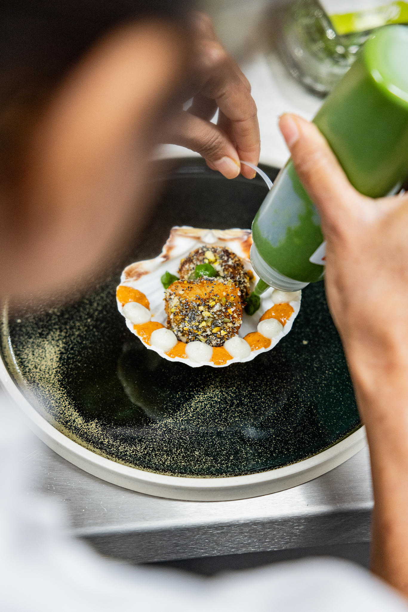 Chef plating a starter at Pravaas — Overhead shot of a chef carefully decorating a plated Indian starter with green sauce.
